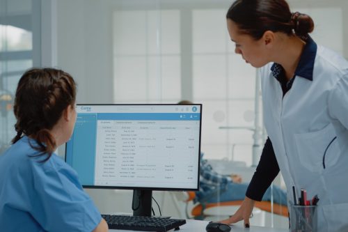 Professional dentist preparing for consultation using x ray from assistant desk at oral clinic. Stomatology nurse working on computer while orthodontist examining patient toothcare